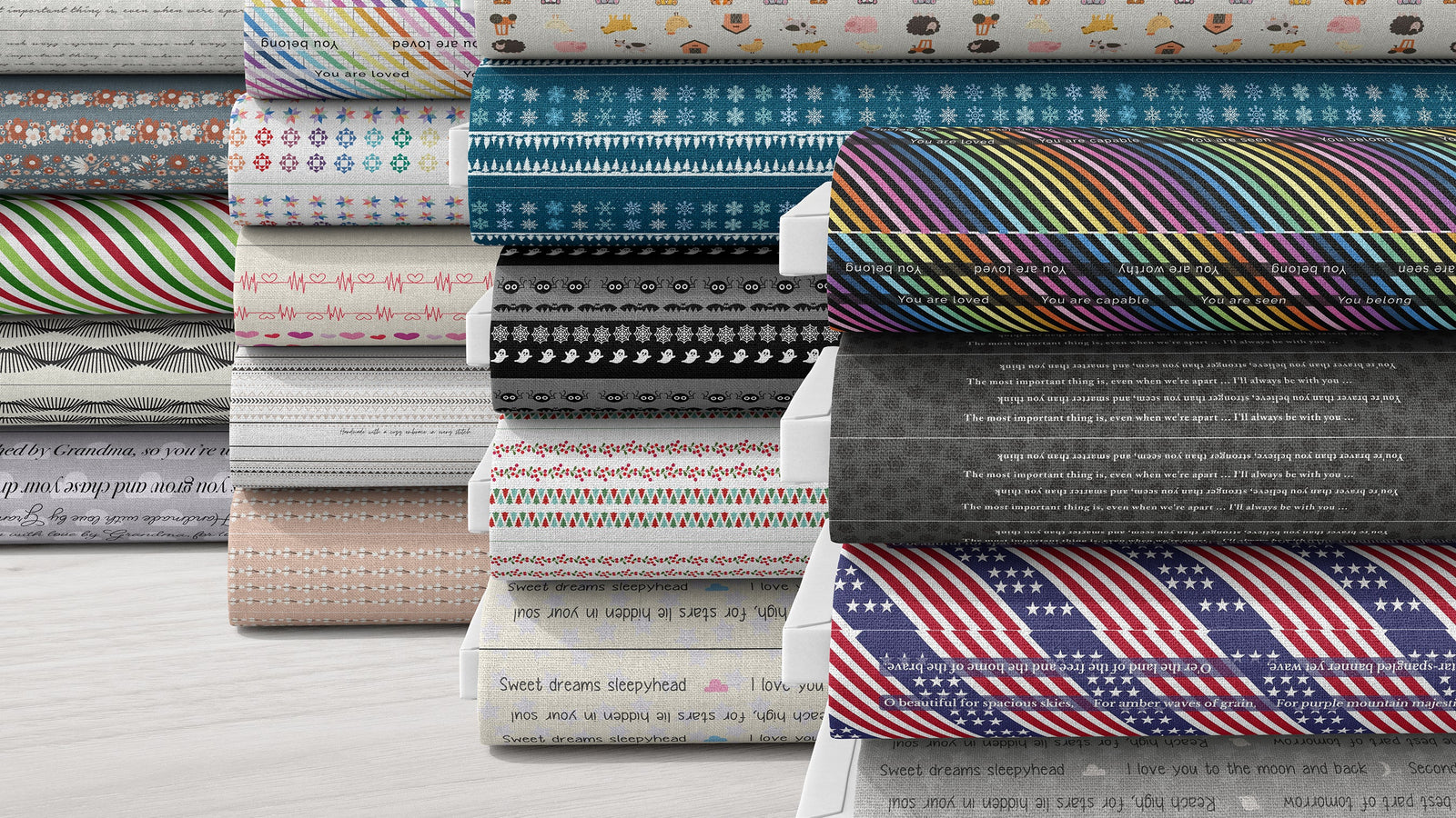 A stack of folded patterned fabric rolls displayed upright on a light wood surface. The fabrics feature various designs including stripes, florals, polka dots, stars, and text prints in multiple colors.